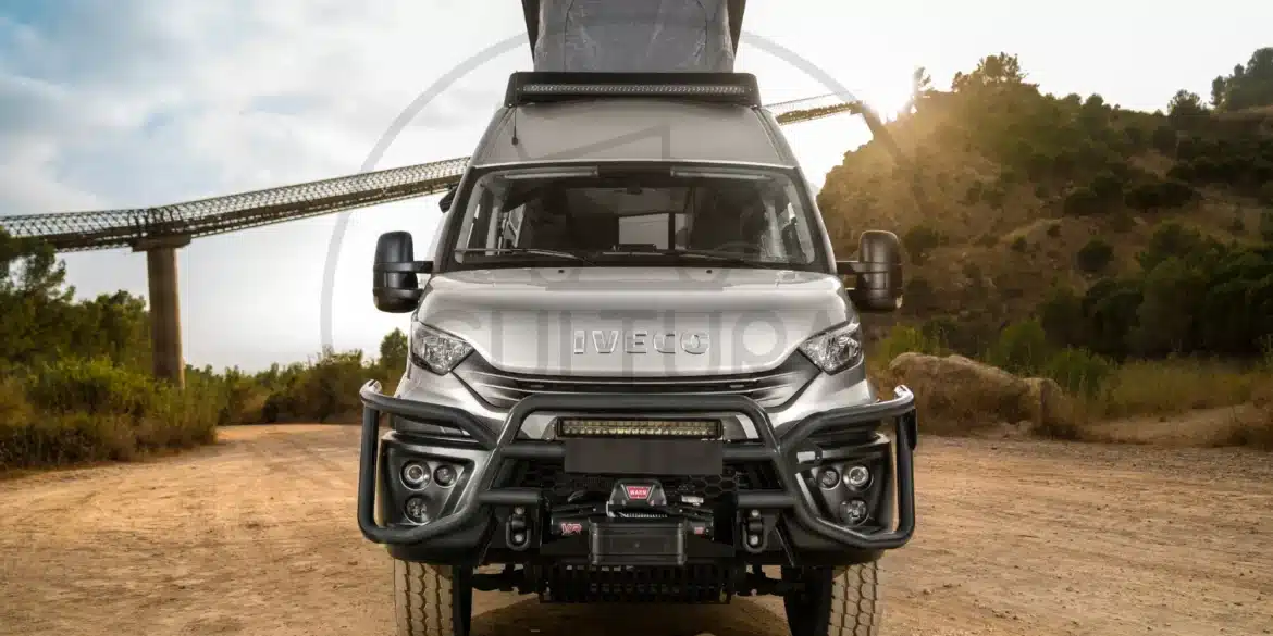 Frontansicht eines silbernen Iveco Daily 4x4 Expeditionscampers mit Offroad-Umbau, aufgestellt auf einer Schotterpiste, Aufstelldach geöffnet.