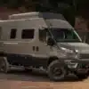 Iveco Daily 4x4 Camperfahrzeug auf sandigem Untergrund vor bewaldeter Kulisse