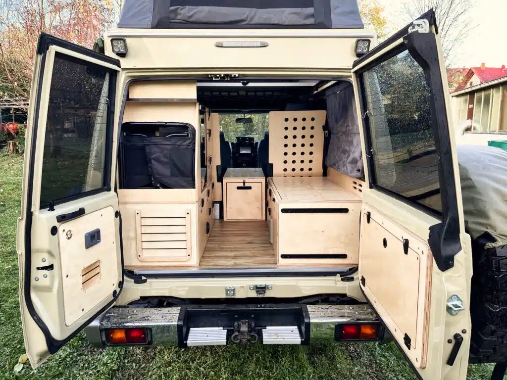 Blick in den ausgebauten Innenraum eines Toyota Land Cruiser 78 mit Hubdach und maßgefertigtem Möbelsystem aus Holz und Stauraumlösungen.