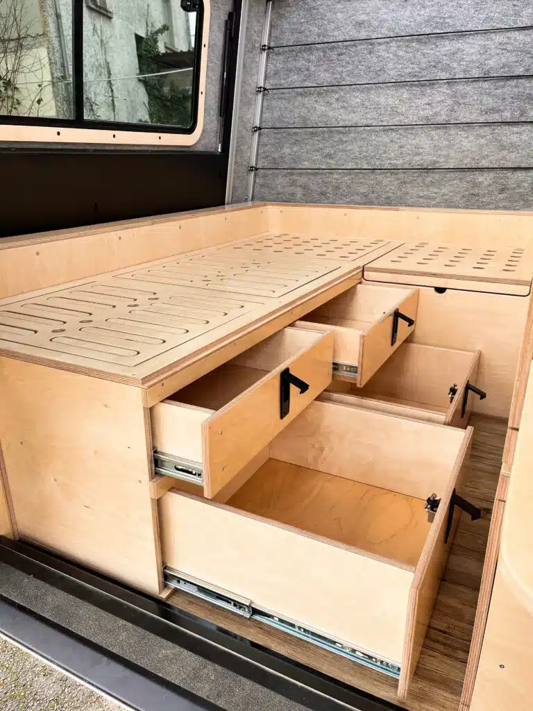 Geöffnete Schubladen unter der Holzsitzbank im Innenausbau eines Defender 130 Pickup Campers.
