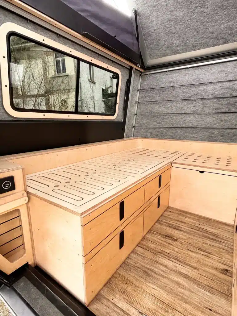 Innenausbau eines Defender 130 Pickup Campers mit L-Sitzgruppe und integrierten Stauraumlösungen aus Holz