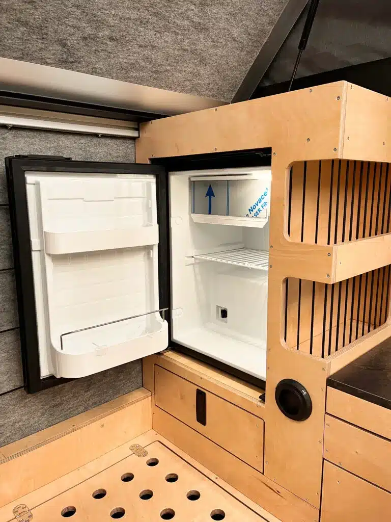 Geöffneter Kühlschrank im Hochschrank des Defender 130 Pickup Camper mit individuellem Innenausbau aus Holz.