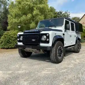 Land Rover Defender Black/White Edition 2015, zum Camper umgebaut, steht vor einem Garten und Haus