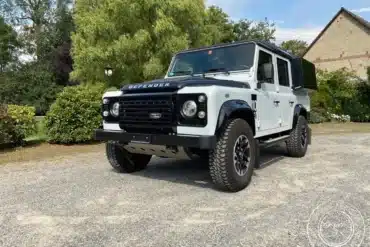 Land Rover Defender Black/White Edition 2015, zum Camper umgebaut, steht vor einem Garten und Haus