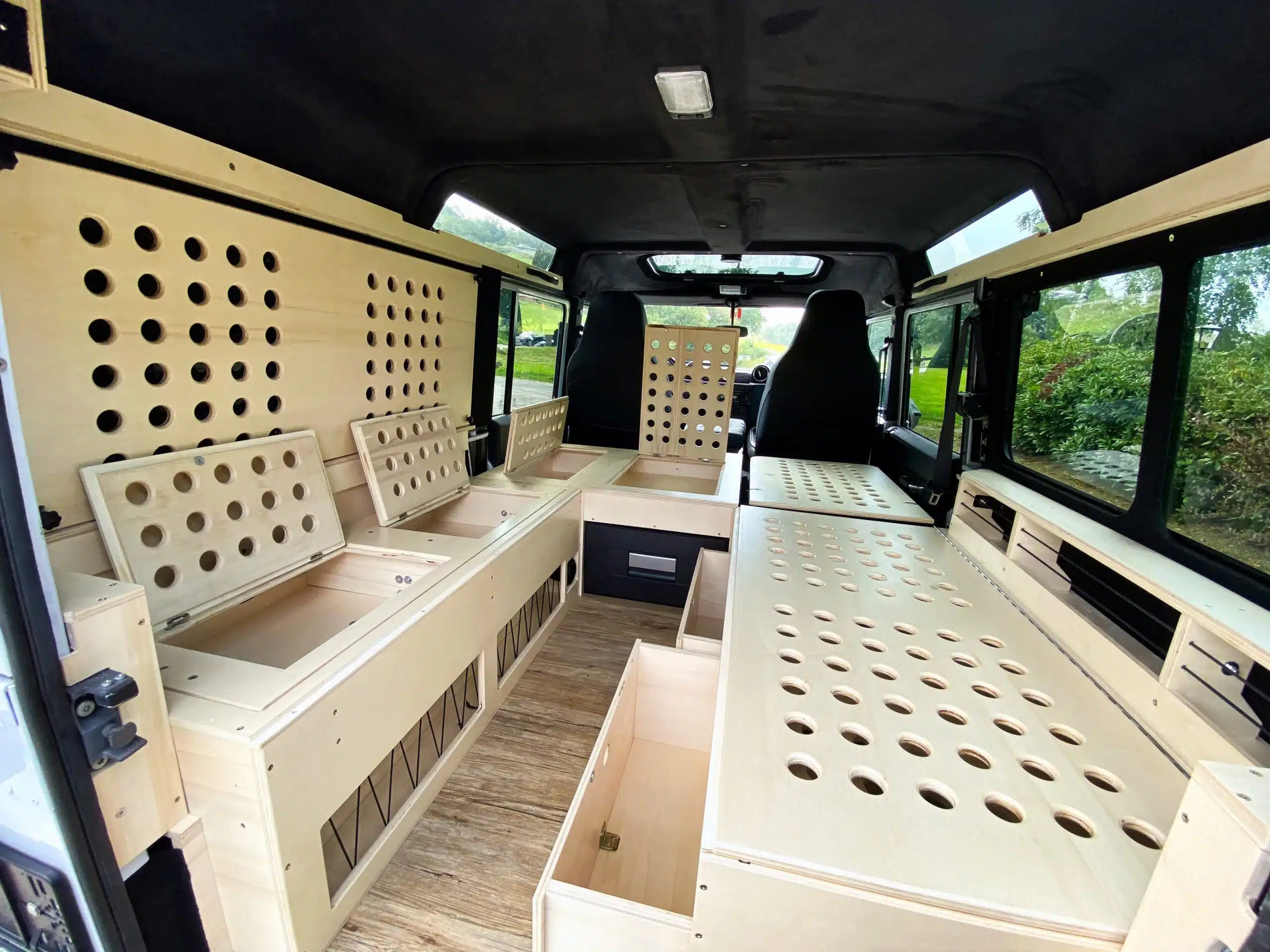 Ausgebauter Innenraum eines Land Rover Defender mit Holzmodulen, Sitzbank, Bett und Stauraum