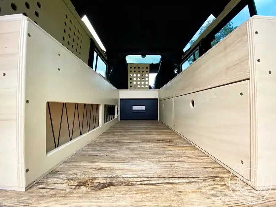 Innenraum eines zum Camper ausgebauten Land Rover Defender mit Holzmodulen, Schubladen und Kompressorkühlschrank