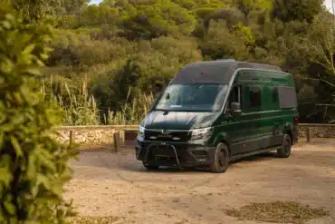 Grüner MAN TGE 4x4 Compass on the Road Campervan mit Hochdach auf einem Stellplatz in naturnaher Umgebung.