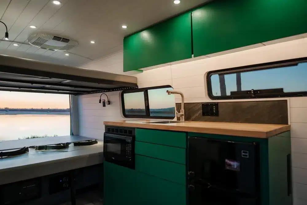 Küchenbereich und Innenraum eines barrierefreien Maverick Sprinter-Campers mit grünen Aluminium-Möbeln und Blick aufs Wasser.