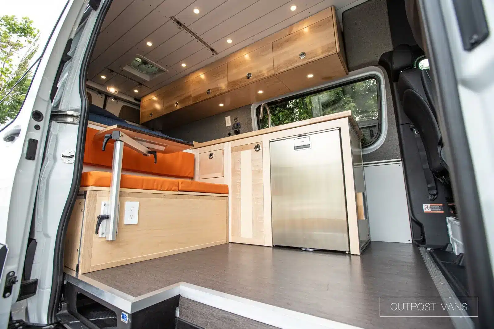 Innenraum eines ausgebauten Mercedes Sprinter Campervans mit Sitzbank, Küche und Stauraum.