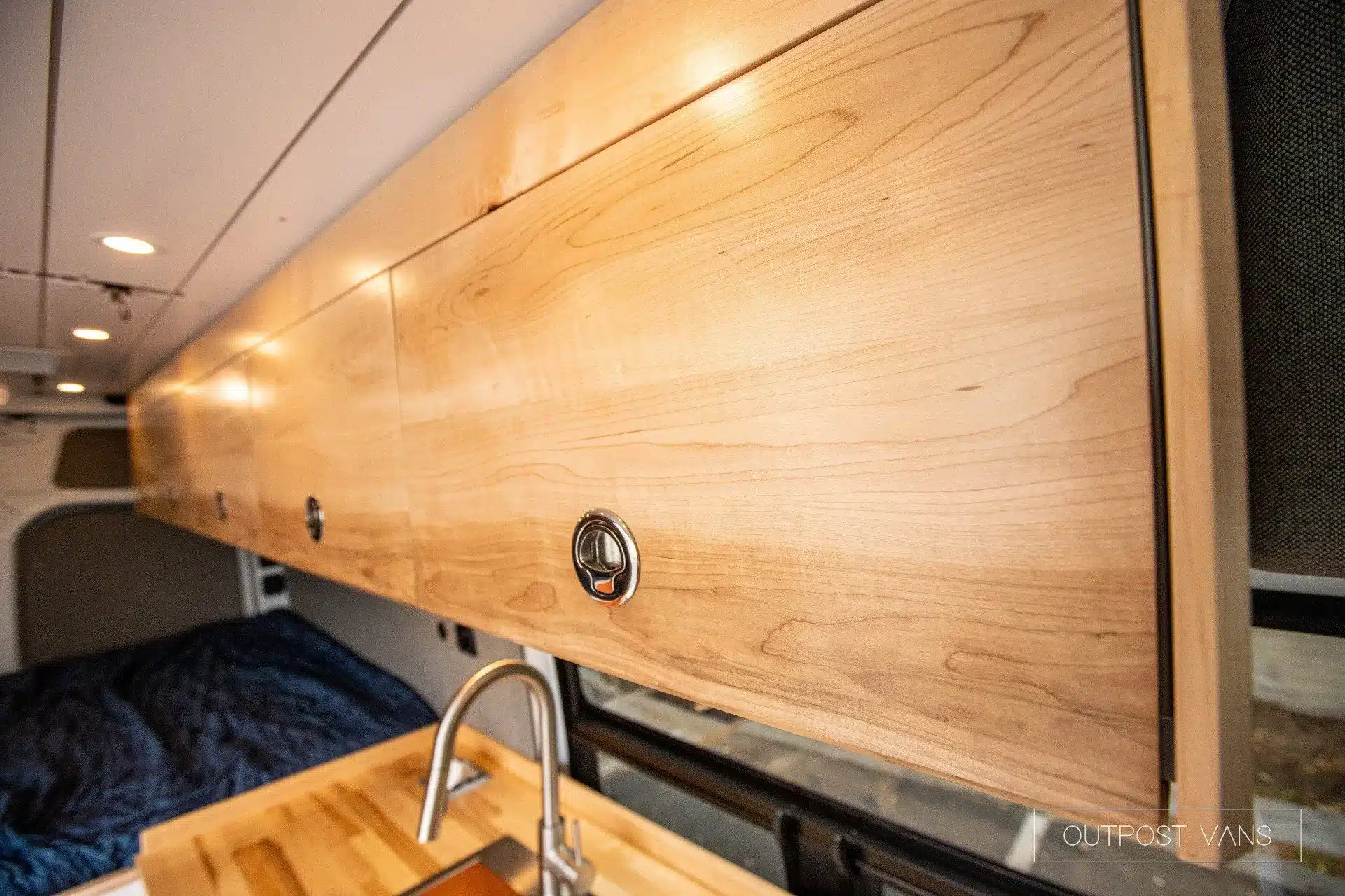 Detailansicht der Ahorn-Hängeschränke und Arbeitsfläche mit Wasserhahn im Mercedes Sprinter Campervan Maple