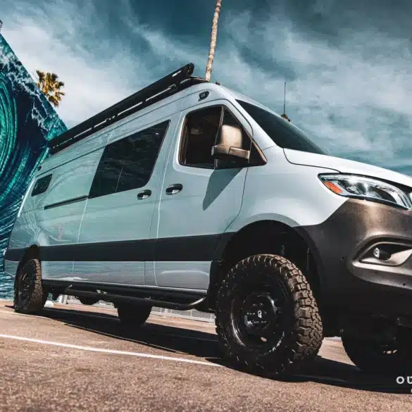 Mercedes Sprinter 4x4 Campervan mit Offroad-Reifen und Dachträger von Outpost Vans vor einer Streetart-Wand mit Surfer.