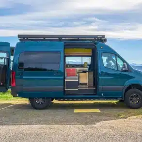 Mercedes Sprinter Camper mit Allradantrieb und modernem Innenausbau, seitlich fotografiert mit geöffneter Tür und Blick auf Küche und Sitzbereich