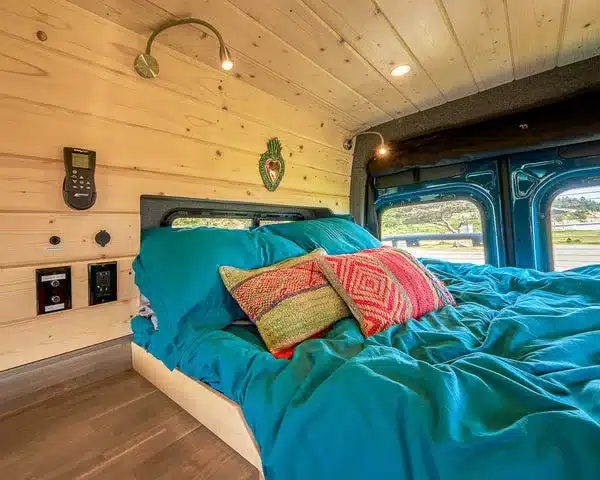 Schlafbereich im ausgebauten Mercedes Sprinter Campervan mit Holzverkleidung, Bett und Kissen.