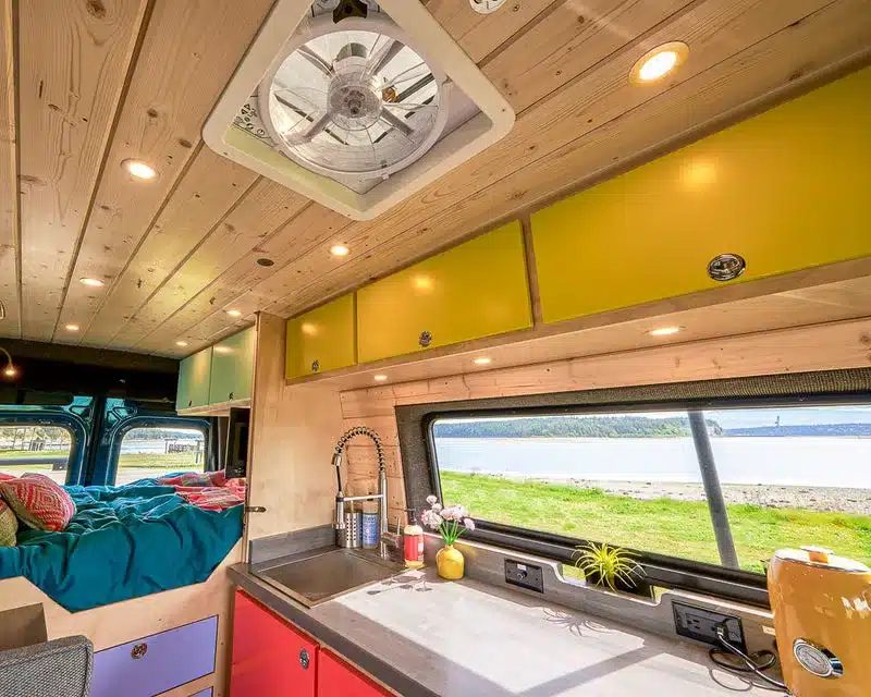 Küchenbereich und Wohnraum eines ausgebauten Mercedes-Benz Sprinter mit Holzverkleidung und Blick nach draußen