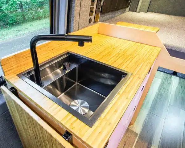 Küchenzeile mit Edelstahlspüle und Holzarbeitsfläche im Mercedes Sprinter Family Van