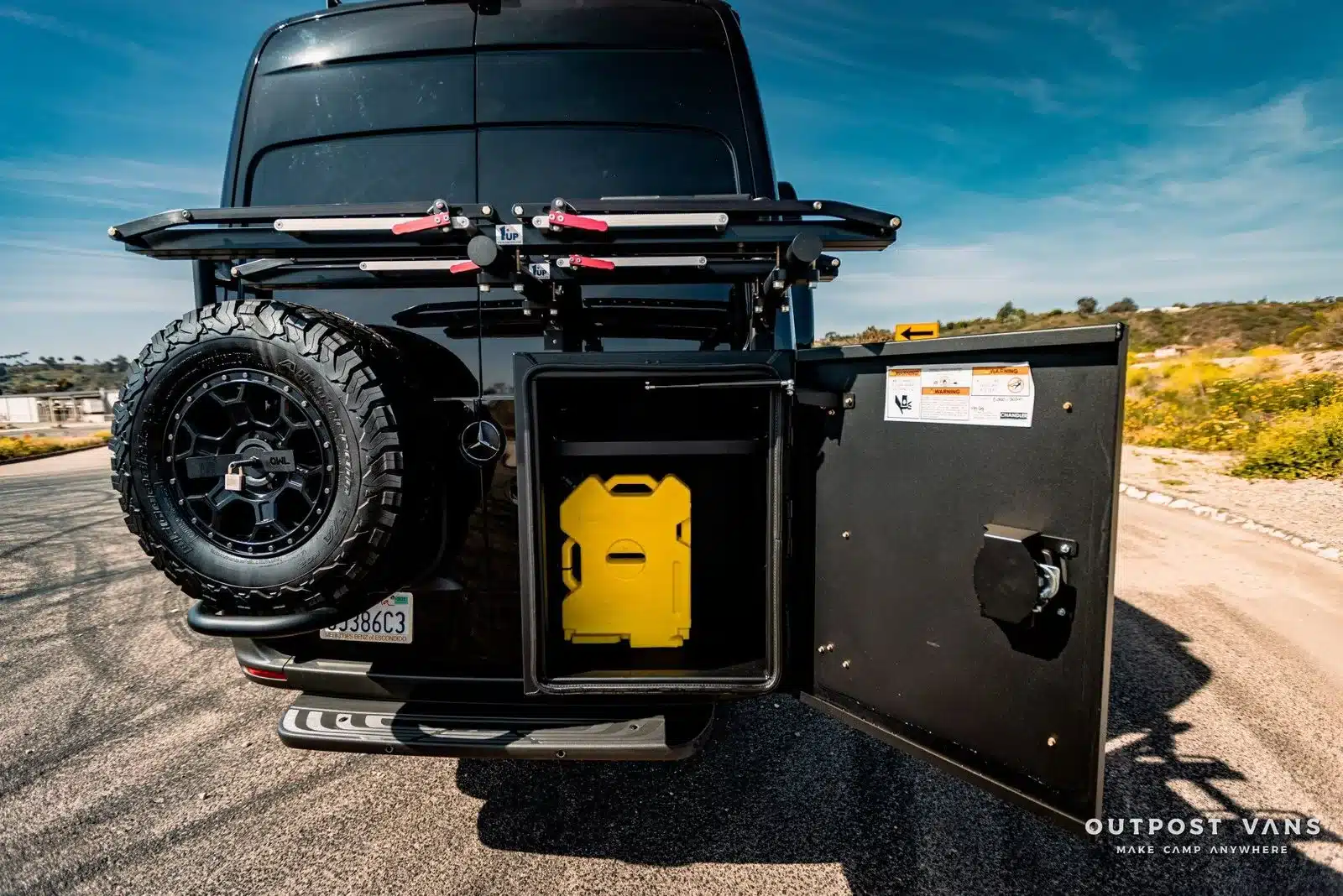 Heckansicht eines aufgerüsteten Mercedes Sprinter Mamba mit Ersatzrad, Fahrradträger und geöffnetem Staufach mit gelbem Wasserkanister
