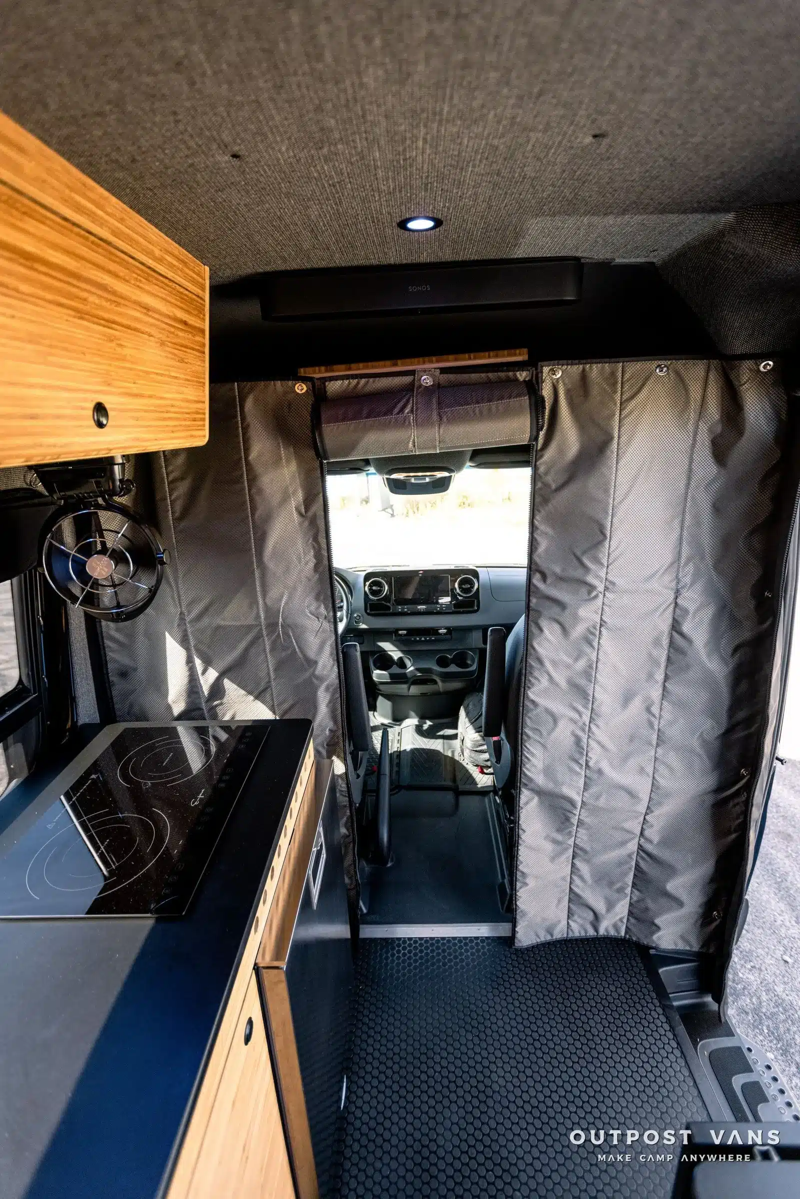 Innenraumansicht eines ausgebauten Mercedes Sprinter Vans mit Küchenzeile, Trennvorhang und Blick ins Cockpit.