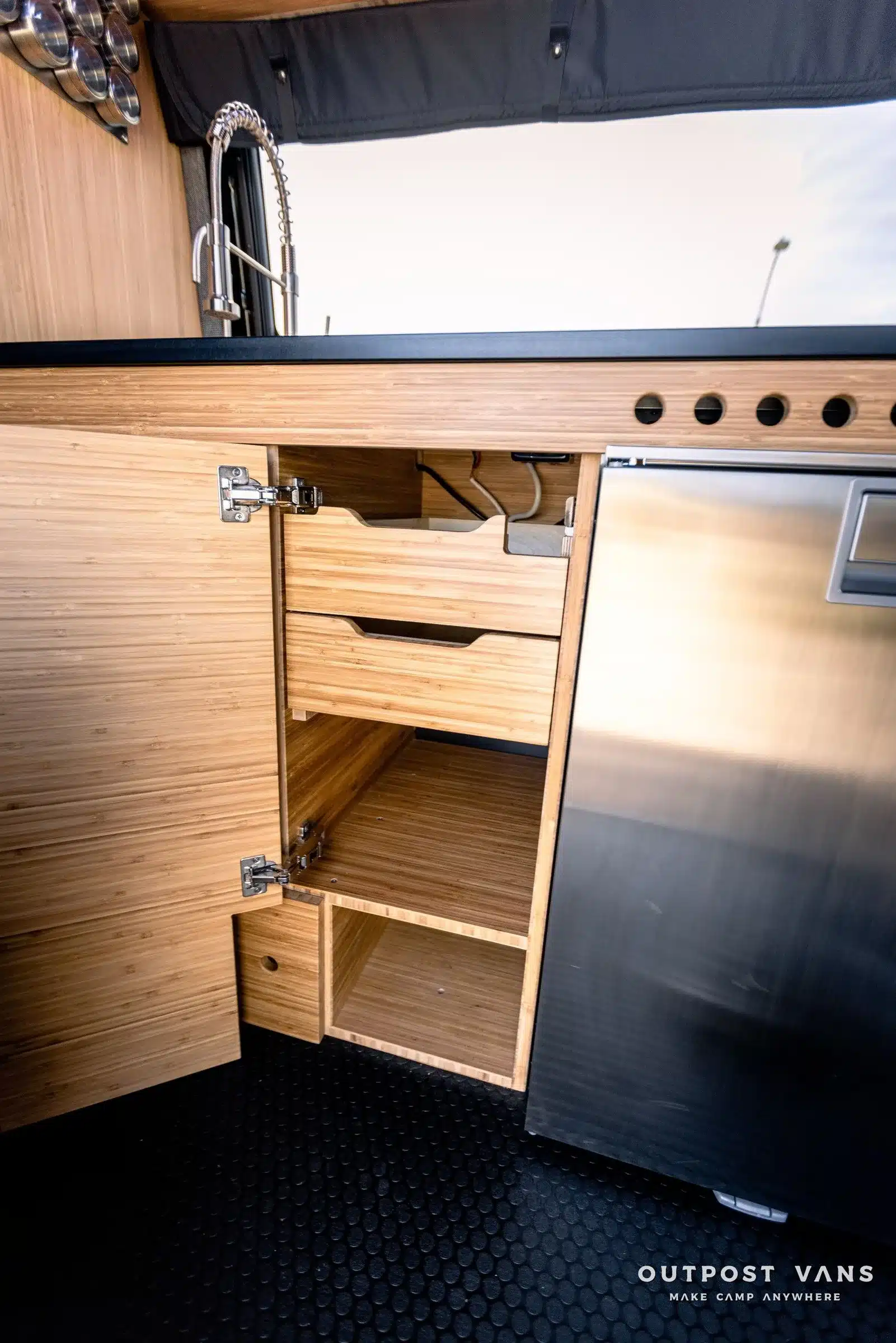 Detailansicht der Küchenzeile mit Edelstahlspüle, Holzschubladen und Kühlschrank im Mercedes Sprinter Mamba Campervan.