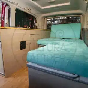 Innenansicht des Mercedes Vito Camper mit seitlicher Möbelzeile, Kompressorkühlschrank und Sitz-/Liegebereich aus türkisfarbenen Polstern.
