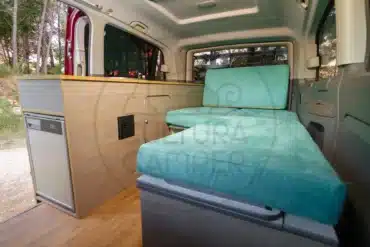 Innenansicht des Mercedes Vito Camper mit seitlicher Möbelzeile, Kompressorkühlschrank und Sitz-/Liegebereich aus türkisfarbenen Polstern.