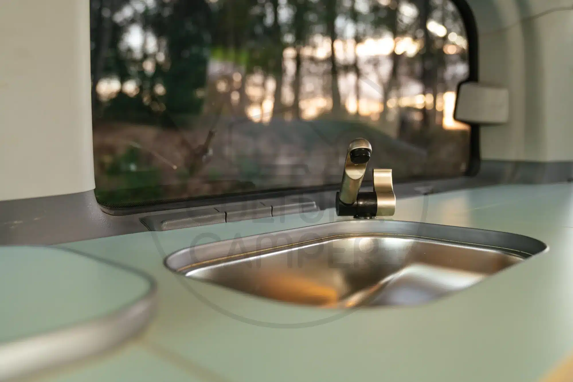 Edelstahlspüle mit Wasserhahn im Innenraum eines Mercedes Vito Campers vor großem Fenster.