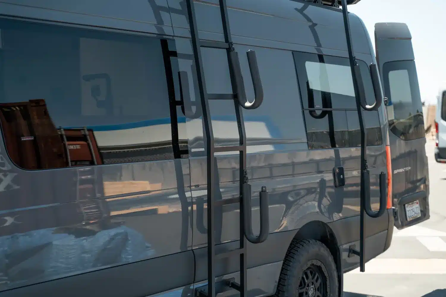 Schwarzer Camper-Van Moose mit montierter Außentrittleiter und Geländebereifung, aufgenommen im Freien.