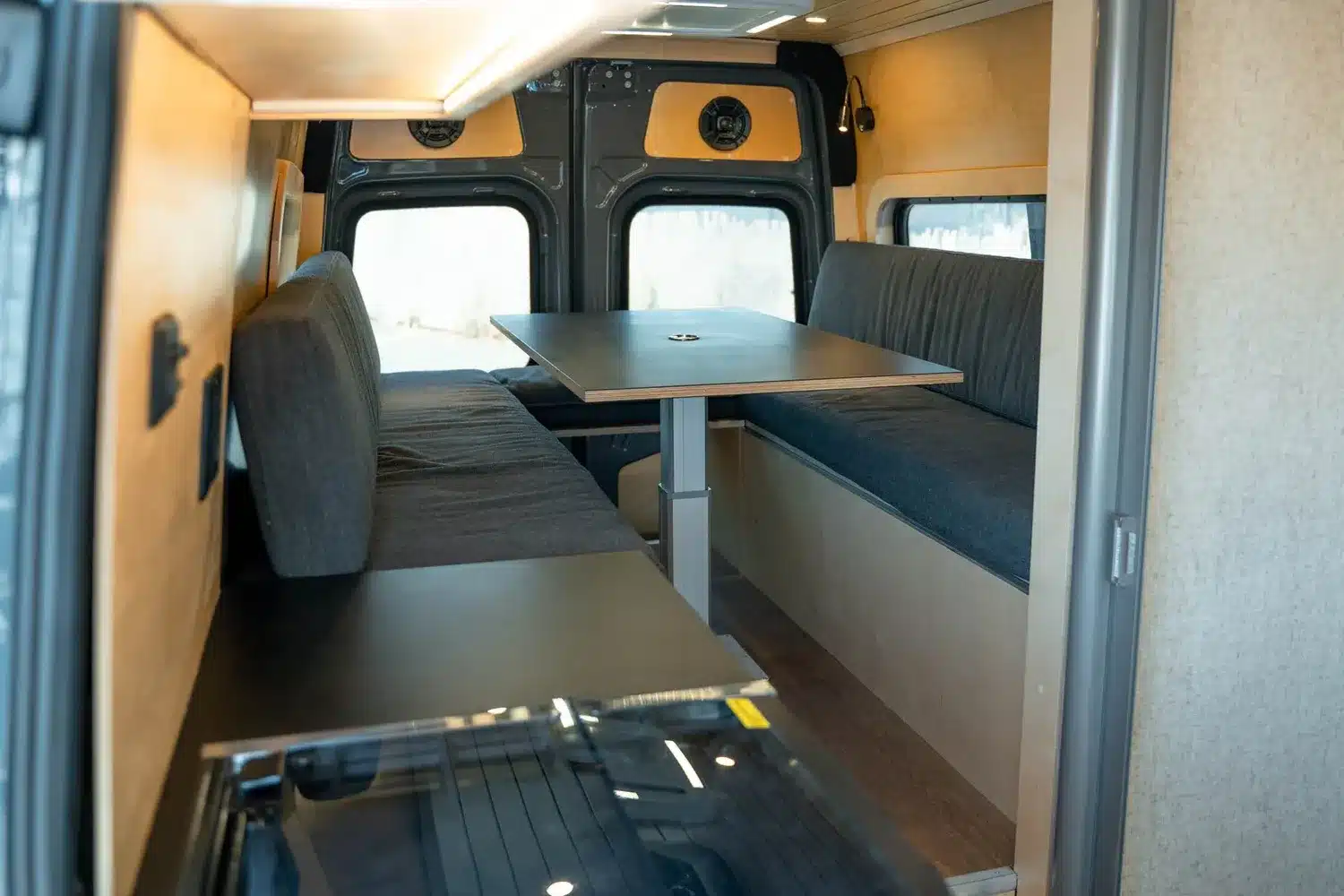 Innenraum des Moose Camper-Ausbaus mit zwei Sitzbänken, großem Tisch und viel Holzverkleidung im nordischen Design.