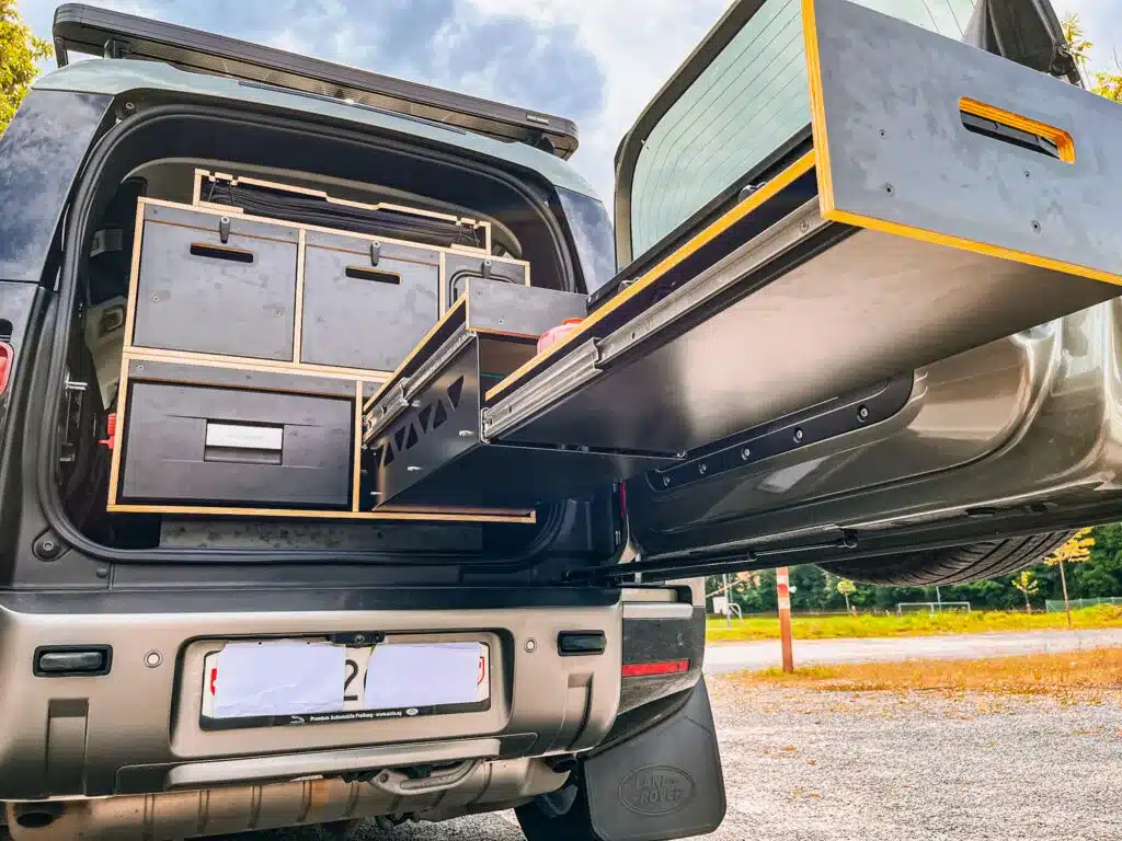 Camping-Ausbau mit Stauboxen und herausgezogenem Küchenmodul im Kofferraum eines Land Rover New Defender