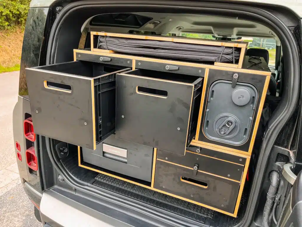 Modulares Camping-Boxensystem im Kofferraum eines New Defender mit ausgezogenen Schubladen und integrierter Kühlbox