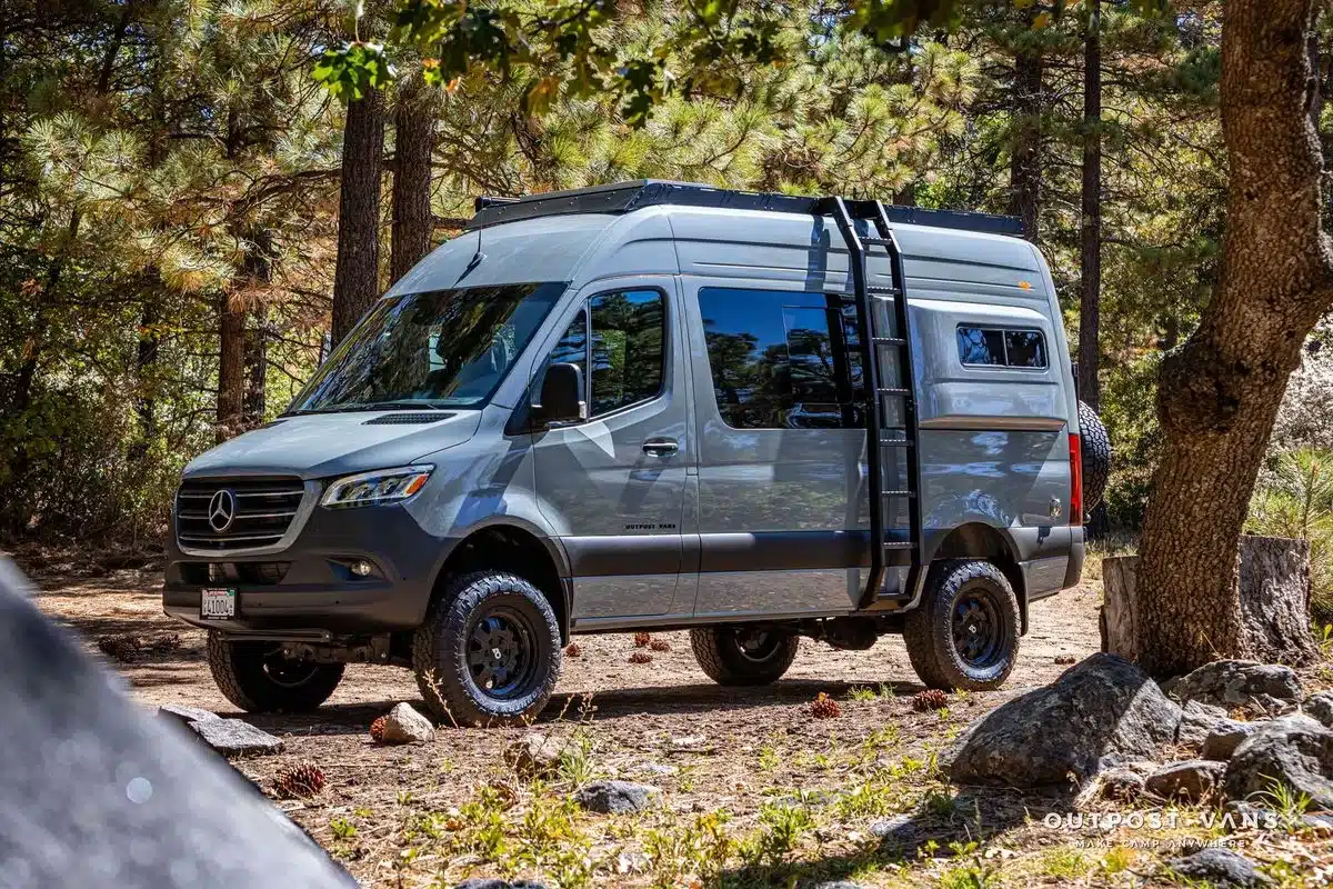 Offroad-Campingbus Outpost Vans CRAG auf Mercedes-Benz Sprinter 144 AWD im Wald, seitliche Ansicht mit Dachträger und Leiter