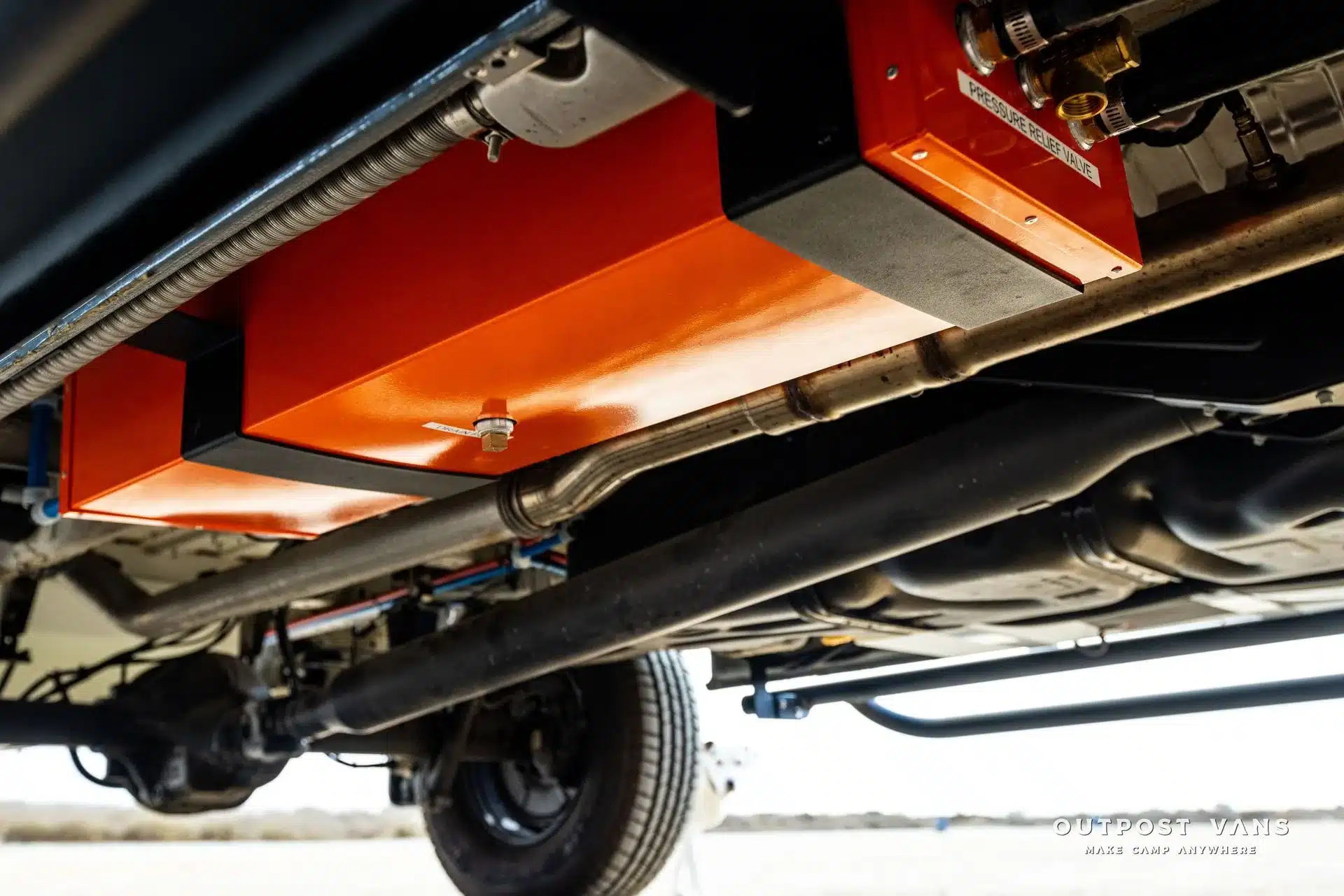 Unterboden mit orangen Technikboxen, Leitungen und Fahrwerk eines Outpost Vans Jasper Campervans