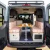 Innenraum eines Outpost Vans Jasper mit Dinette-Sitzgruppe im Heck, fotografiert durch die offenen Hecktüren.