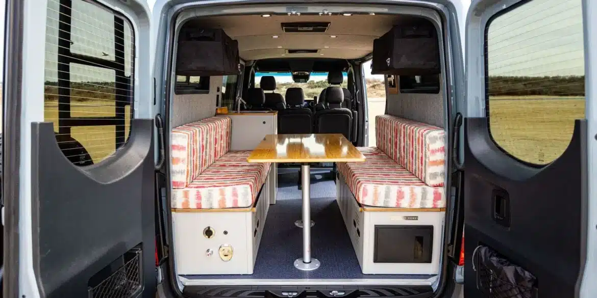 Innenraum eines Outpost Vans Jasper mit Dinette-Sitzgruppe im Heck, fotografiert durch die offenen Hecktüren.