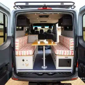 Innenraum eines Outpost Vans Jasper mit Dinette-Sitzgruppe im Heck, fotografiert durch die offenen Hecktüren.