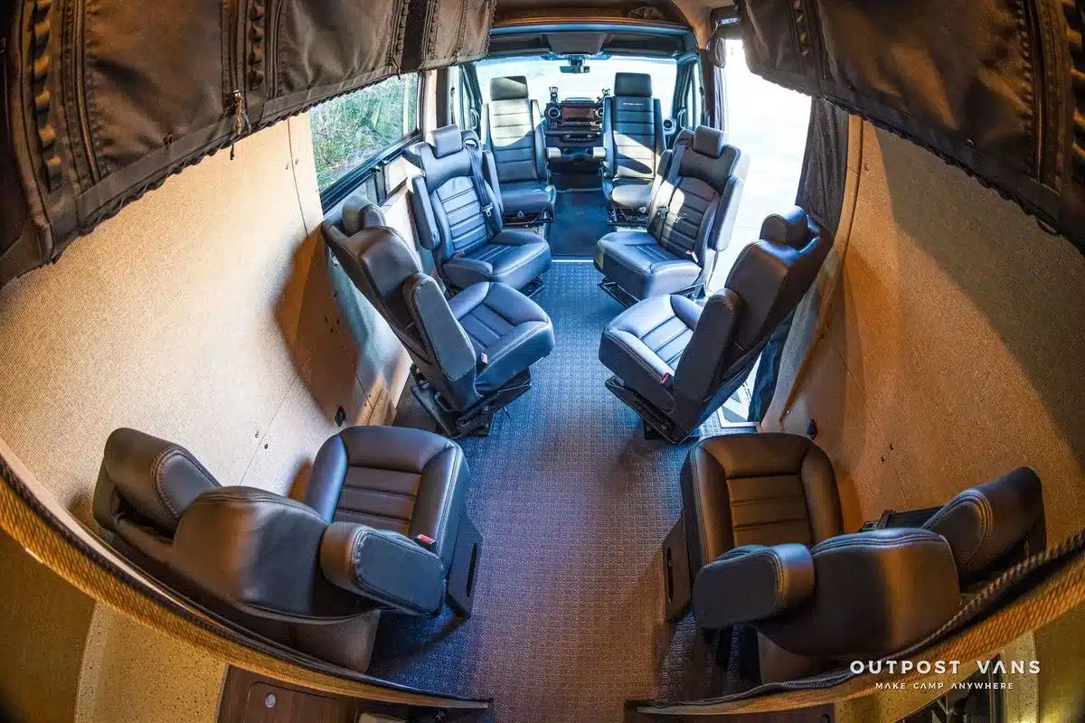 Innenraum eines Outpost Vans LOBO mit acht schwarzen Einzelsitzen auf flexiblen Schienen im Mercedes Sprinter