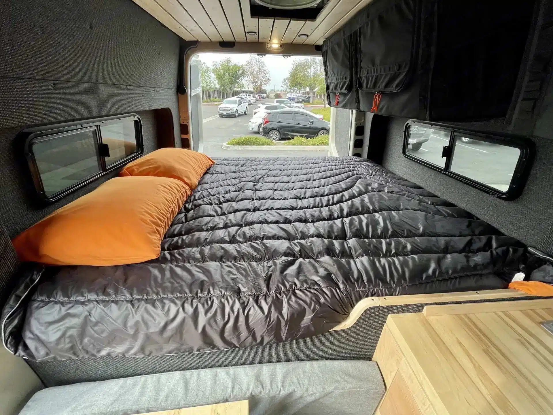 Blick in den Innenraum eines Outpost Vans OPV-04 mit großem Bett, orangen Kissen und Stauraum