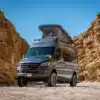 Der Outpost Vans PELE Campervan, basierend auf dem Mercedes Sprinter 144 High Roof mit geöffnetem Aufstelldach, steht in einer felsigen Wüstenumgebung.