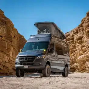 Der Outpost Vans PELE Campervan, basierend auf dem Mercedes Sprinter 144 High Roof mit geöffnetem Aufstelldach, steht in einer felsigen Wüstenumgebung.