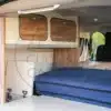 Innenansicht eines umgebauten Peugeot Expert oder Traveller mit integriertem Möbelbau, Klappbett und Stauraum.