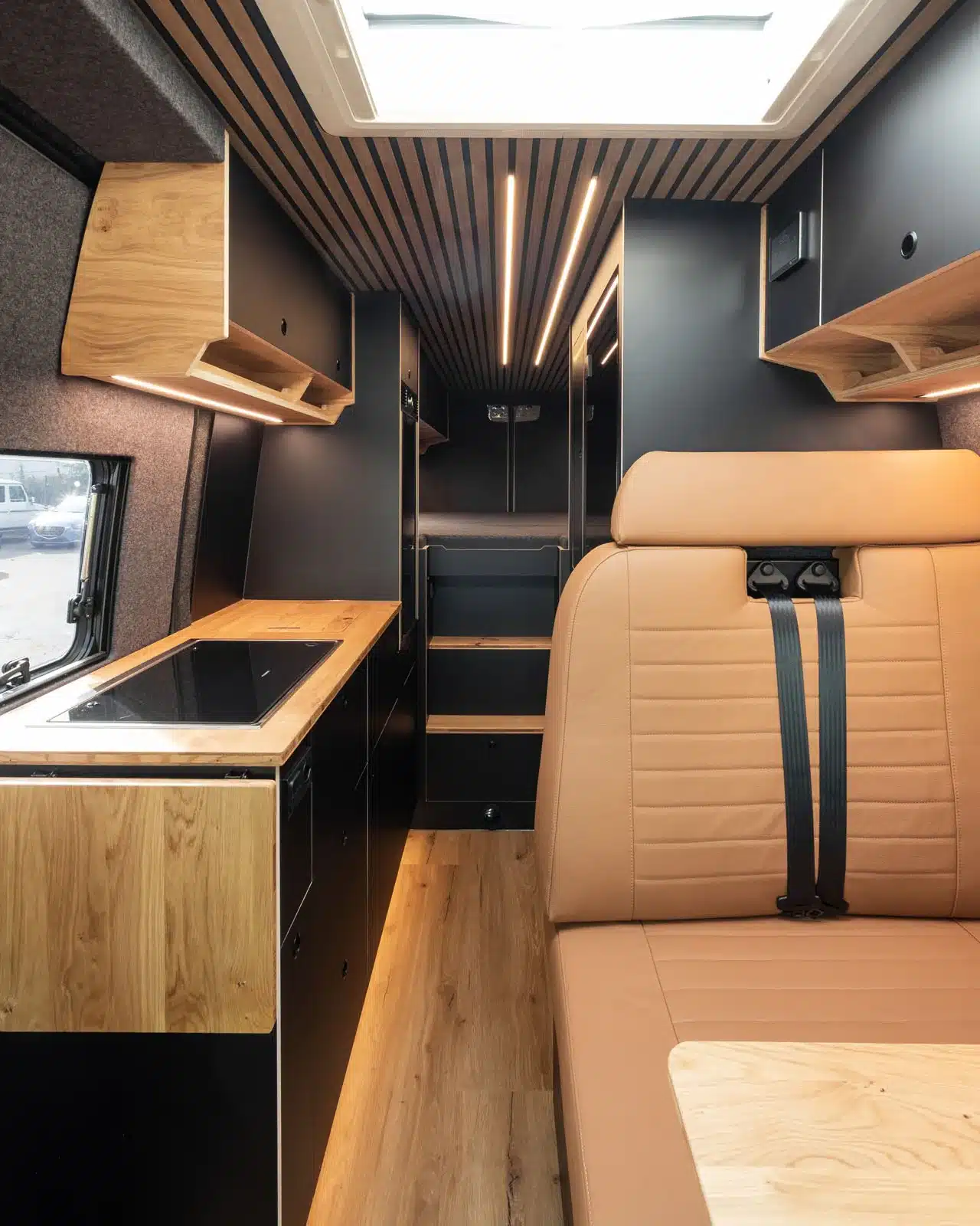Modernes Interieur eines Campers auf Mercedes Sprinter Basis mit Ledersitzen, Echtholzarbeitsfläche, Hängeschränken und festen Schlafplätzen.