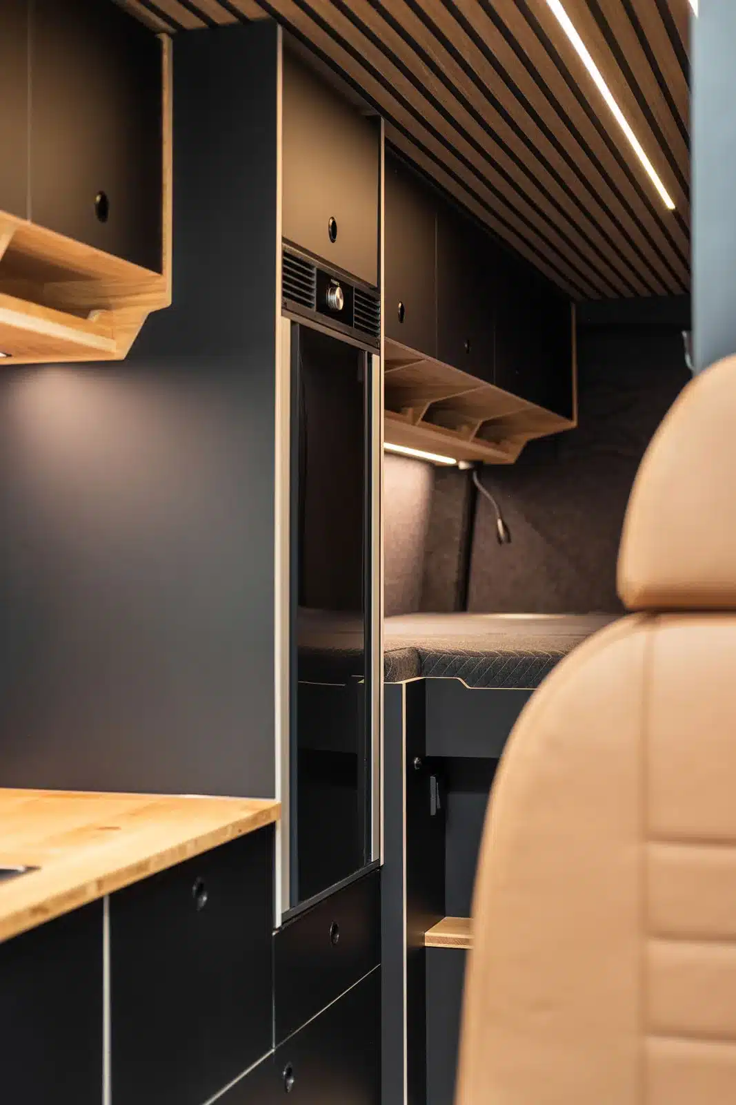Innenansicht eines hochwertig ausgebauten Mercedes Sprinter Campervans mit Längsbett, schwarzen Möbeln und Holzdekor.