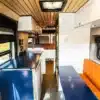 Blick in den stilvollen Innenraum eines Ram Promaster Altitude Campervans mit moderner Küche, Lounge-Sitzbank und festem Bett.