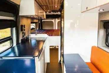 Blick in den stilvollen Innenraum eines Ram Promaster Altitude Campervans mit moderner Küche, Lounge-Sitzbank und festem Bett.