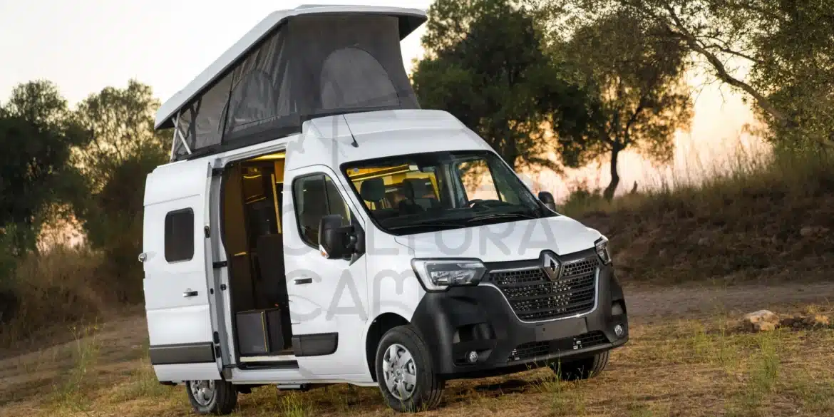 Renault Master L1H2 Camper mit geöffnetem Aufstelldach und geöffneter Schiebetür, geparkt im Grünen bei Sonnenuntergang.
