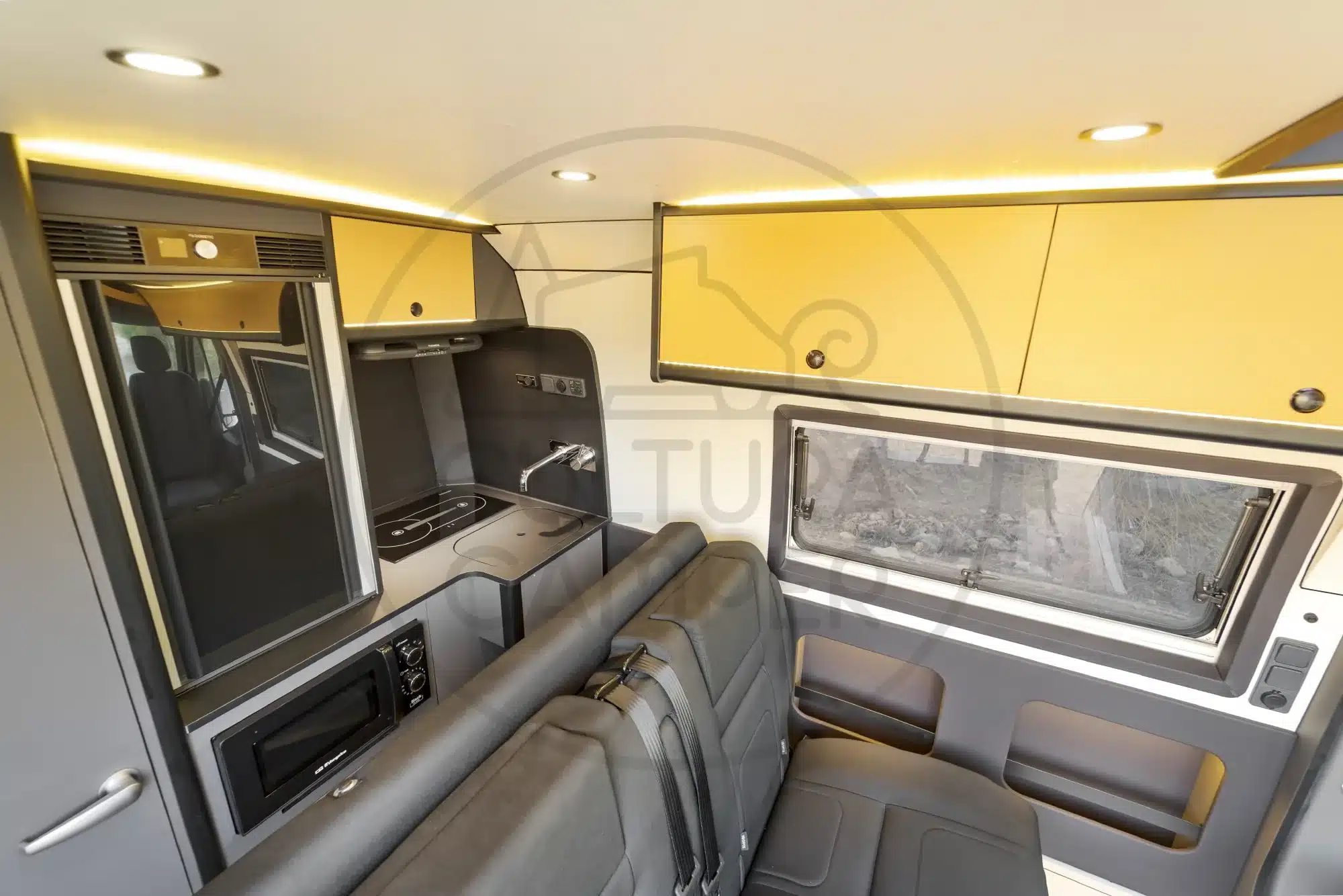 Innenraum eines Renault Master L1H2 Campers mit gelben Oberschränken, Sitzbank, Küche, Fenster und LED-Beleuchtung.