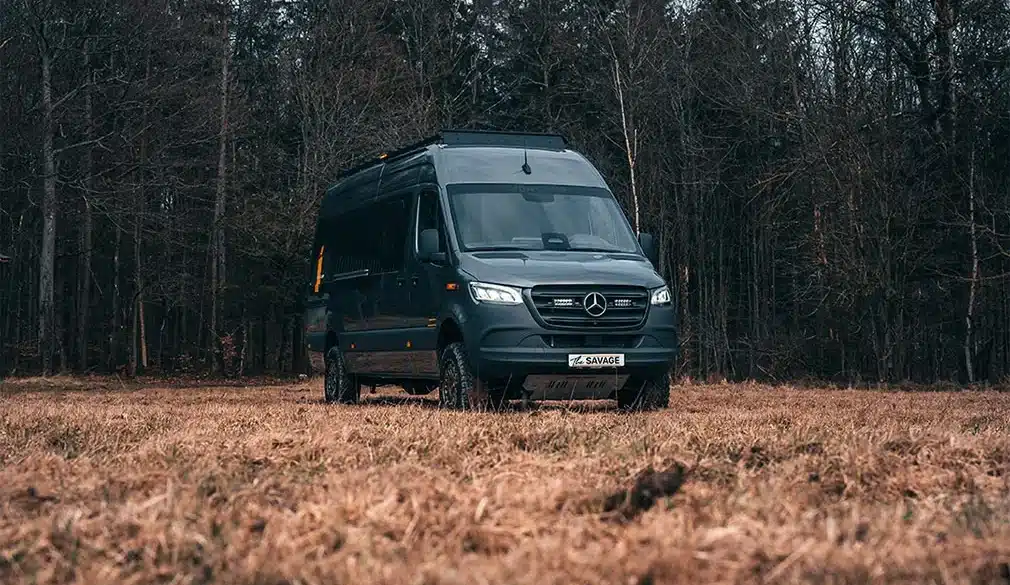 Rhön Camp THE SAVAGE Campervan auf Mercedes Sprinter Basis steht auf einer Lichtung vor Bäumen
