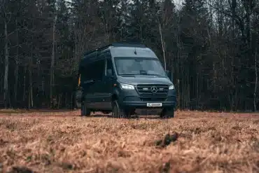 Rhön Camp THE SAVAGE Campervan auf Mercedes Sprinter Basis steht auf einer Lichtung vor Bäumen