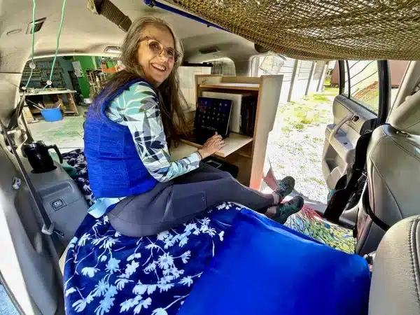 Frau sitzt im umgebauten Innenraum eines Toyota Highlander SUV mit Camping-Ausbau und nutzt einen integrierten Klapptisch zum Arbeiten