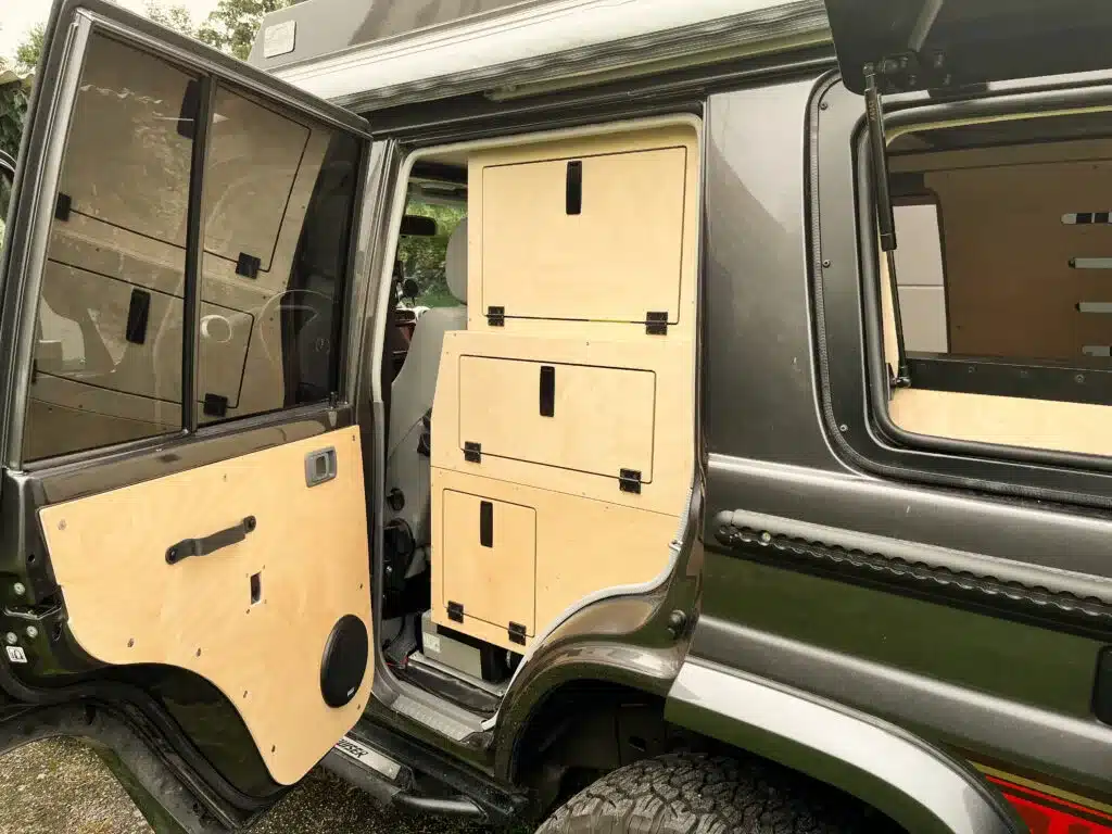 Geöffnete Tür und maßgeschneiderte Holzstauboxen im Innenraum eines ausgebauten Toyota Land Cruiser 76.