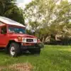 Roter Toyota Land Cruiser BJ45 mit ausgefahrenem Hubdach als Campingfahrzeug auf einer Wiese